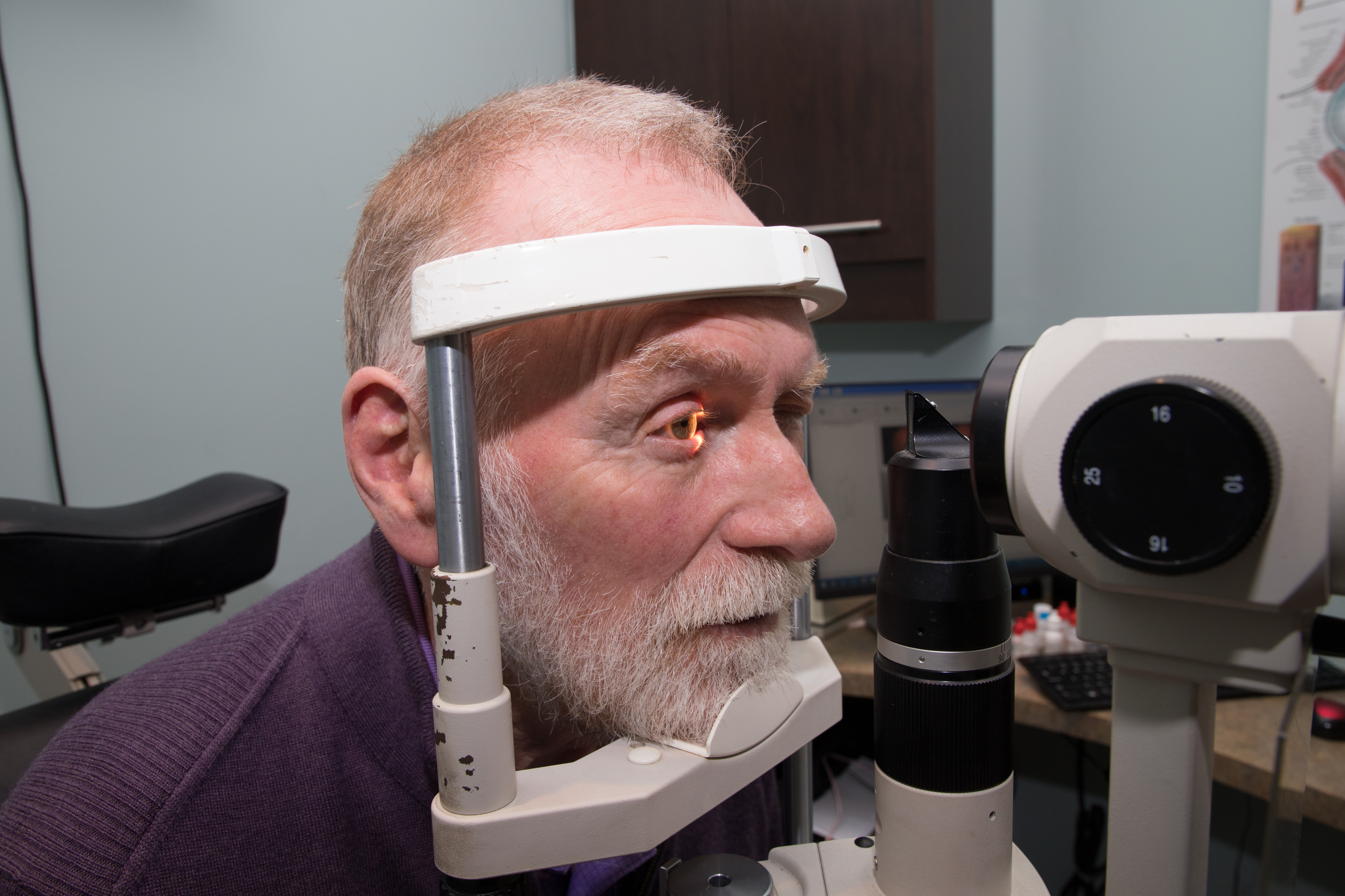 Older man having his eye checked, with light on his right eye