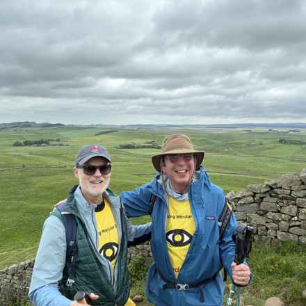 David and Tord in macular tshirts and wearing walking gear, smiling at the camera with a view of a large field and rolling hills in the background 