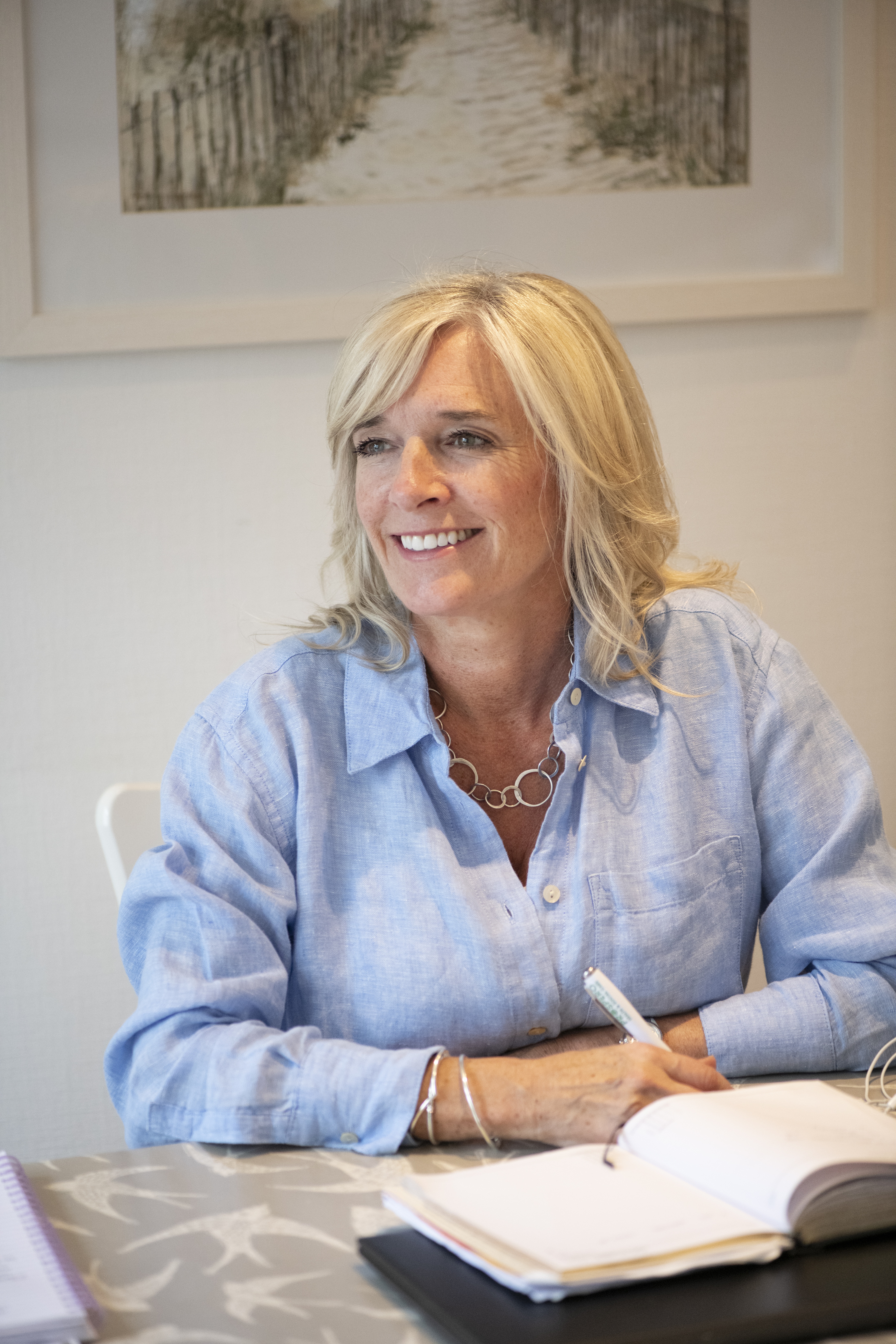 Macular Society counsellor Suzanne, a white woman with blonde hair wearing a light blue shirt and looking into the distance smiling. 