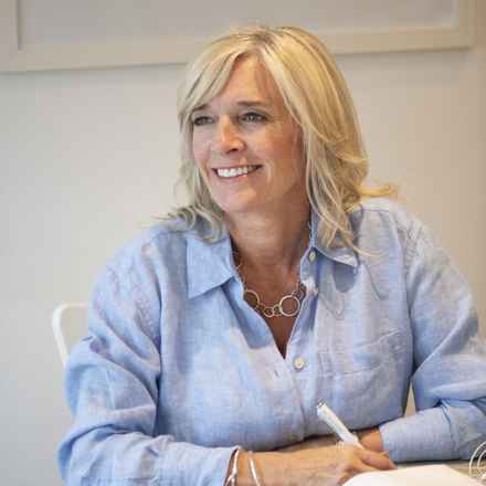 Macular Society counsellor Suzanne, a white woman with blonde hair wearing a light blue shirt and looking into the distance smiling. 