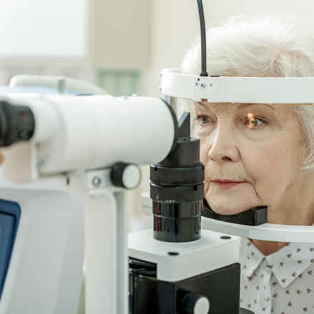 Elderly woman leaning into eye examination machine.