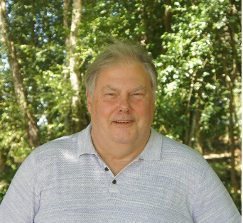 Head and shoulders picture of Dave a white man wearing a shirt with greenery in the background 