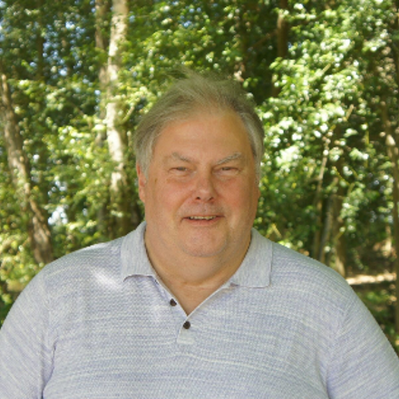 Head and shoulders picture of Dave a white man wearing a shirt with greenery in the background 