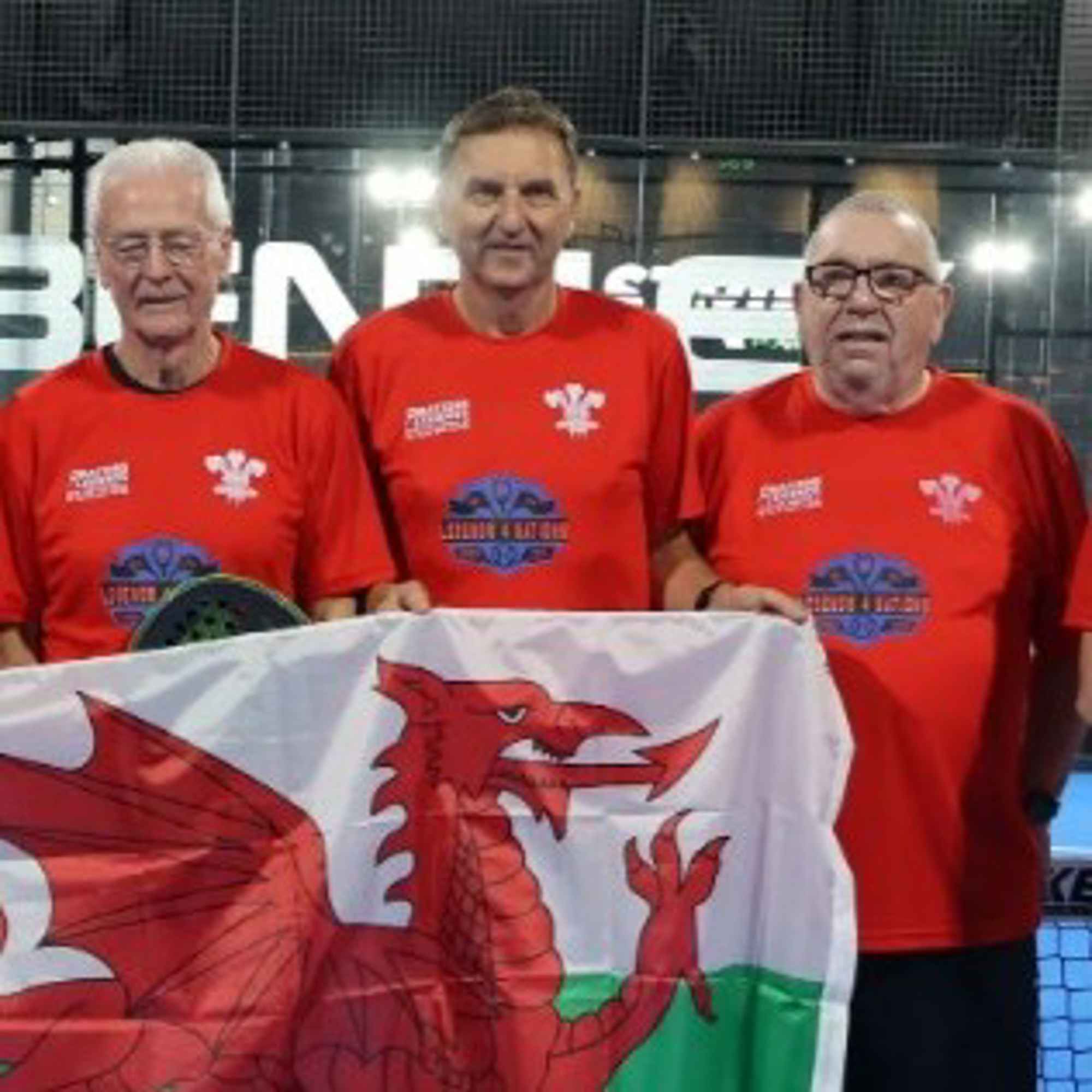 Paul, on the far right next to two of his senior Wales padel teammates, standing behind the Welsh national flag 