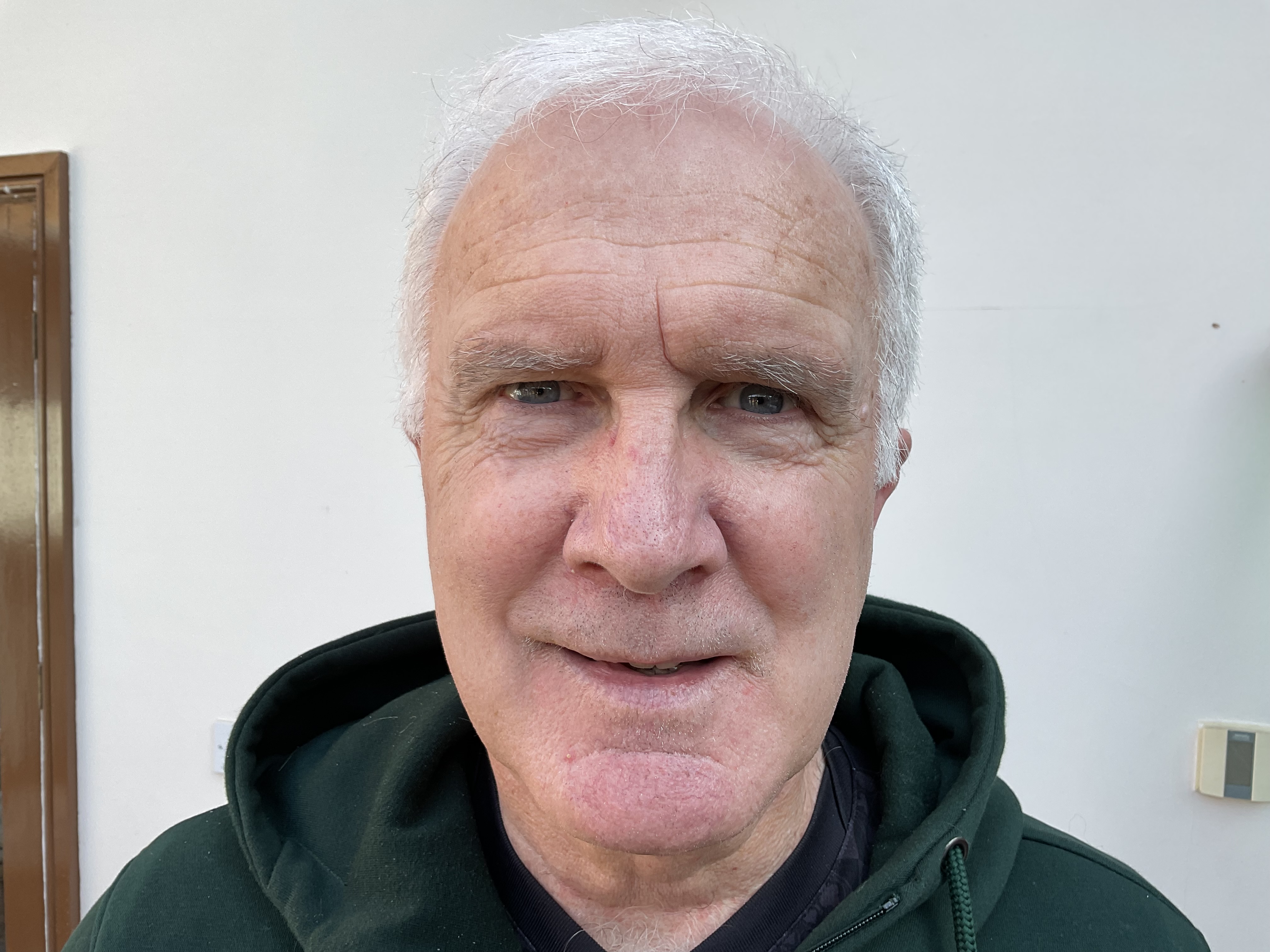 a head and shoulders photo of Alan, a white man in his 70s with grey hair, smiling at the camera 