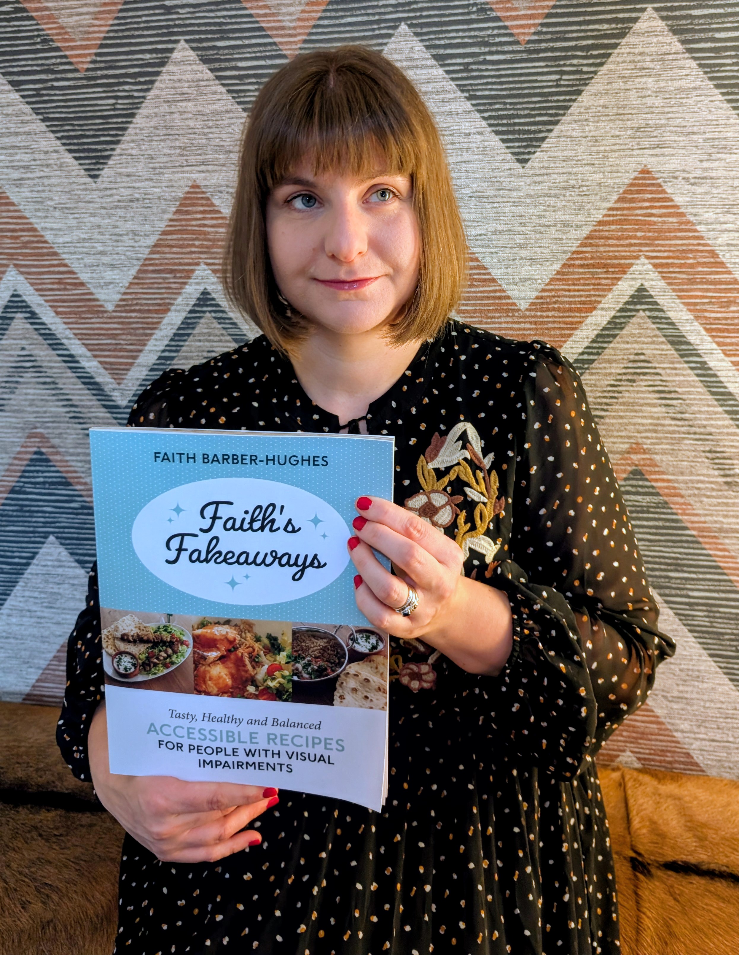 Faith a white woman in her 30s with short brown hair and a fringe smiling and holding a copy of her new cookbook 