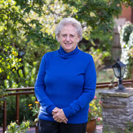 Vera wearing a blue jumper standing in her garden