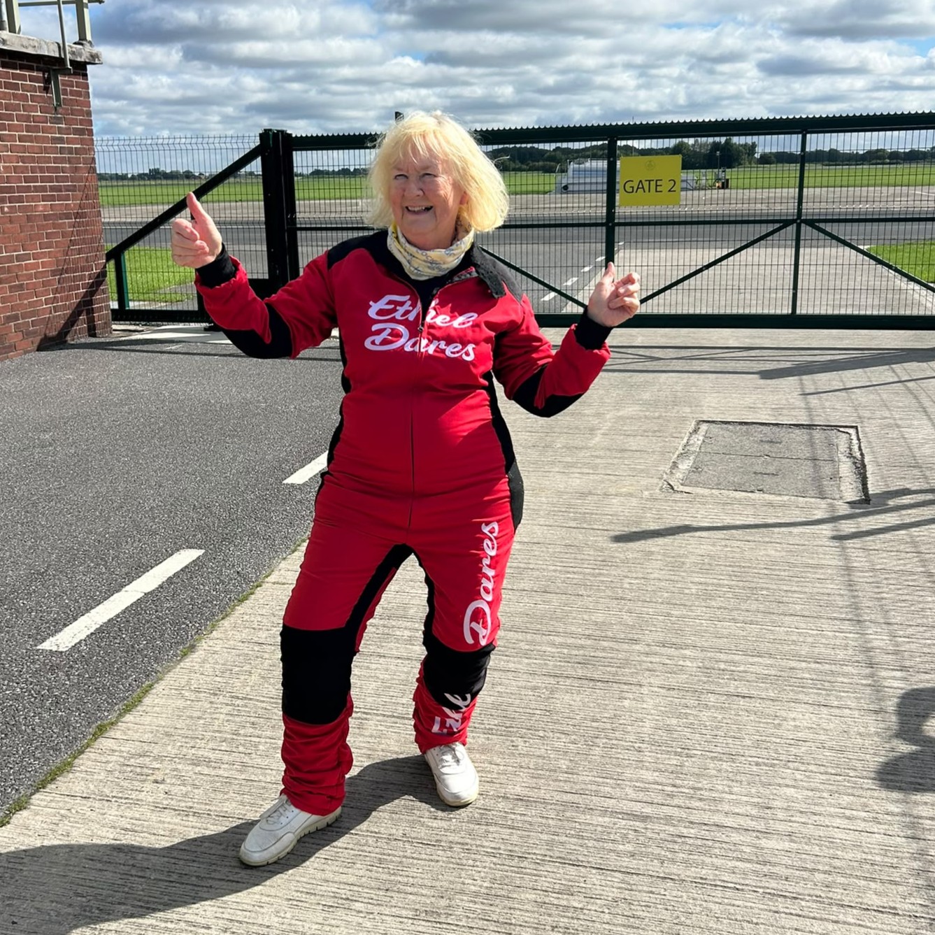 Janet dressed in her red flying jumpsuit is all smiles with her thumbs up