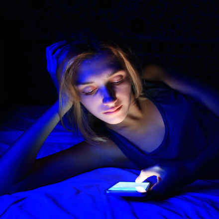 A woman looking at her phone in the dark with blue light