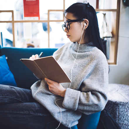 Woman listening to audiobook while writing in book