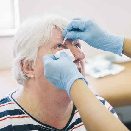 Eye drops being instilled into patient by professional with blue gloves.