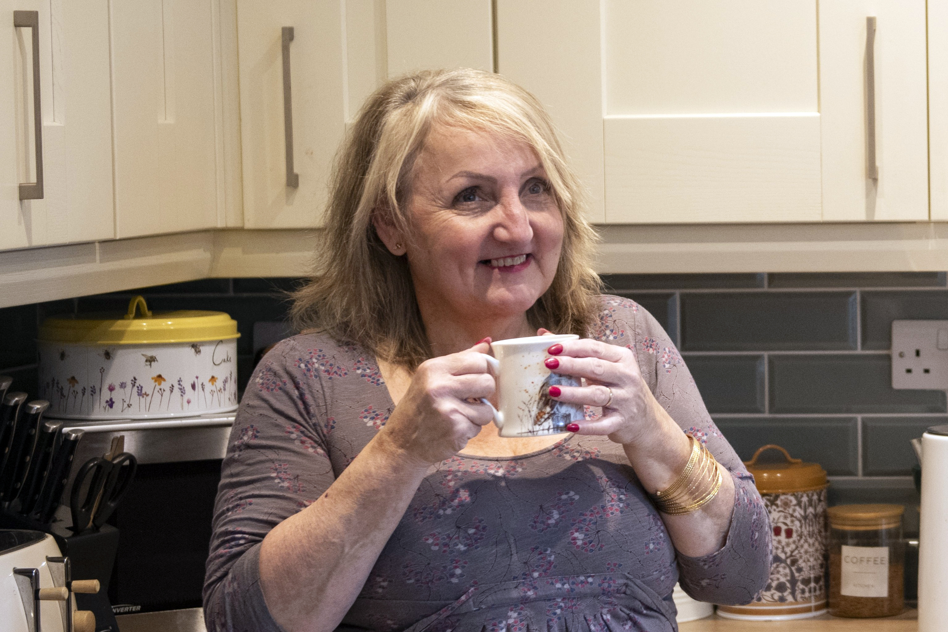 Sue smiling with a cup of tea and looking off into the distance